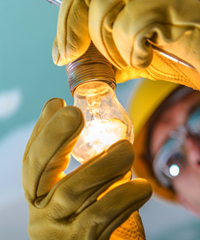 Electrician wearing safety gloves and hard hat installing a light bulb, professional electrical services and lighting installation.